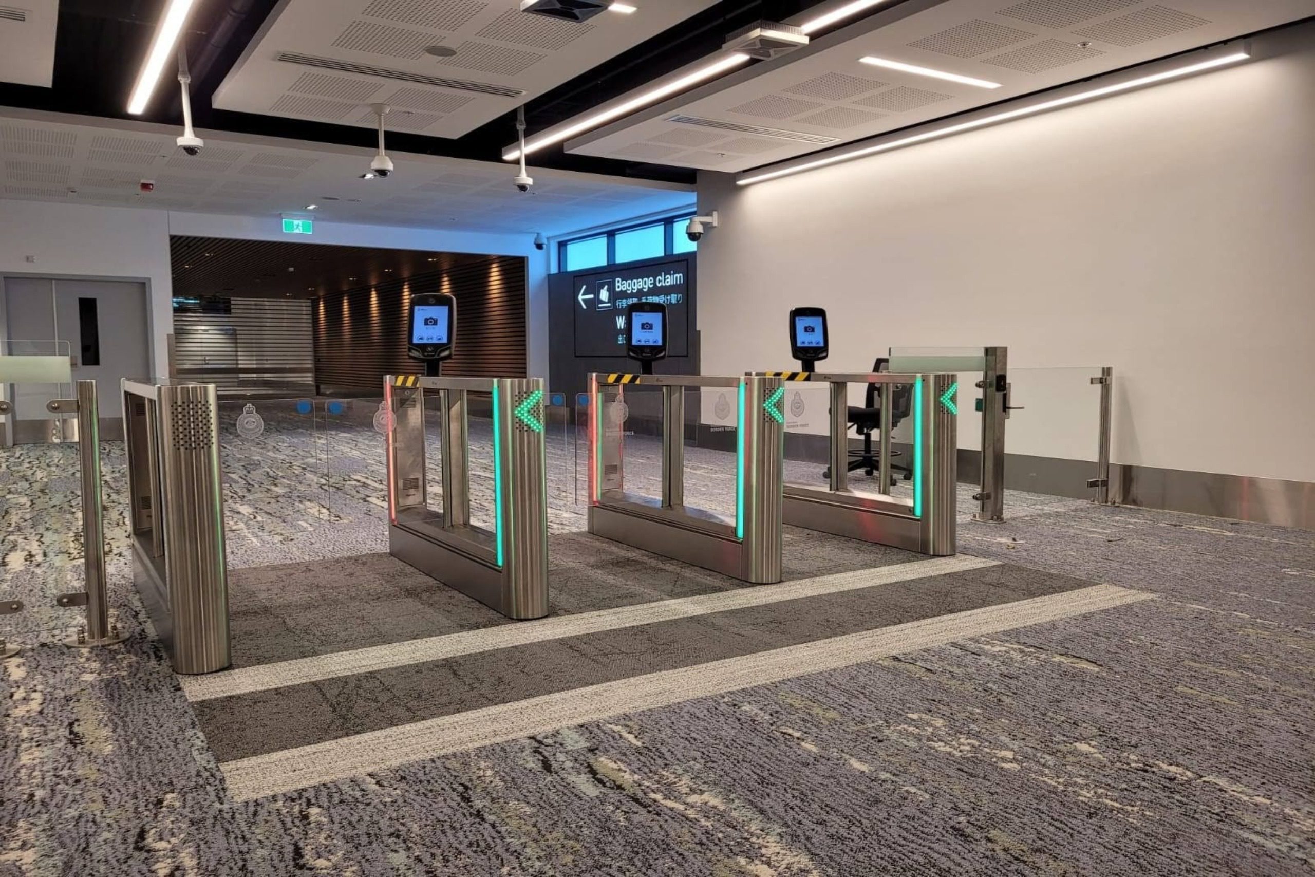 Een rij moderne doorloopsluizen met glazen panelen, groene pijlen en gezichtherkenningsterminals op standaarden, een biometrische toegangsoplossing voor een drukke openbare ruimte zoals een vliegveld.